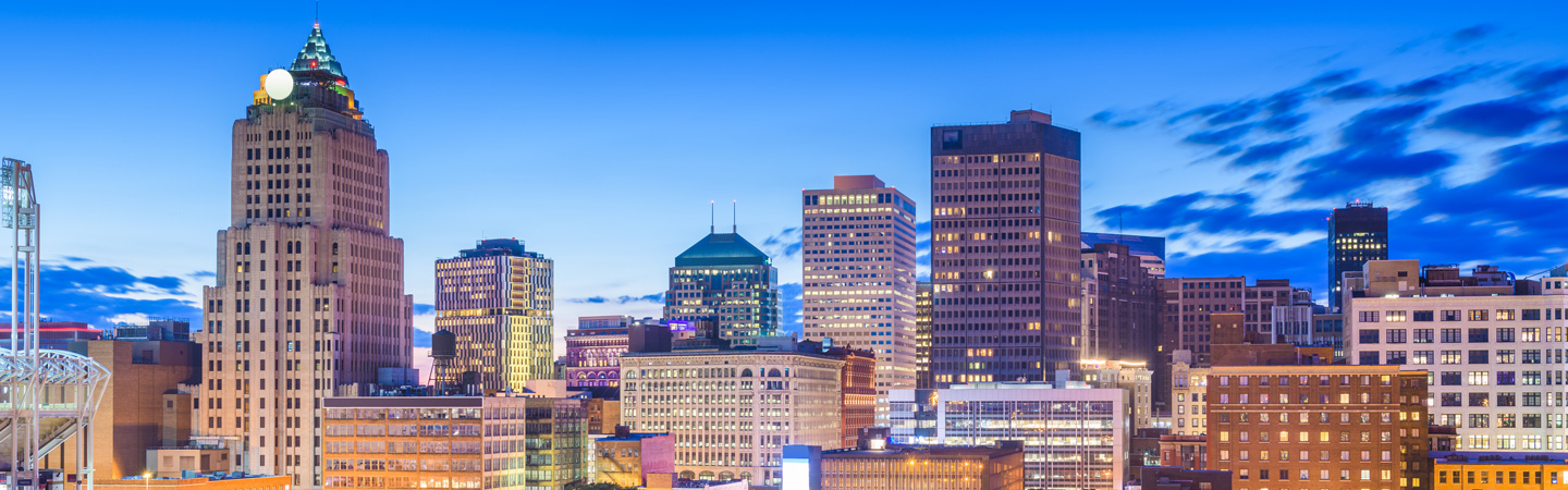 Skyline of a cityscape at dusk featuring tall buildings with a clear blue sky in the background.