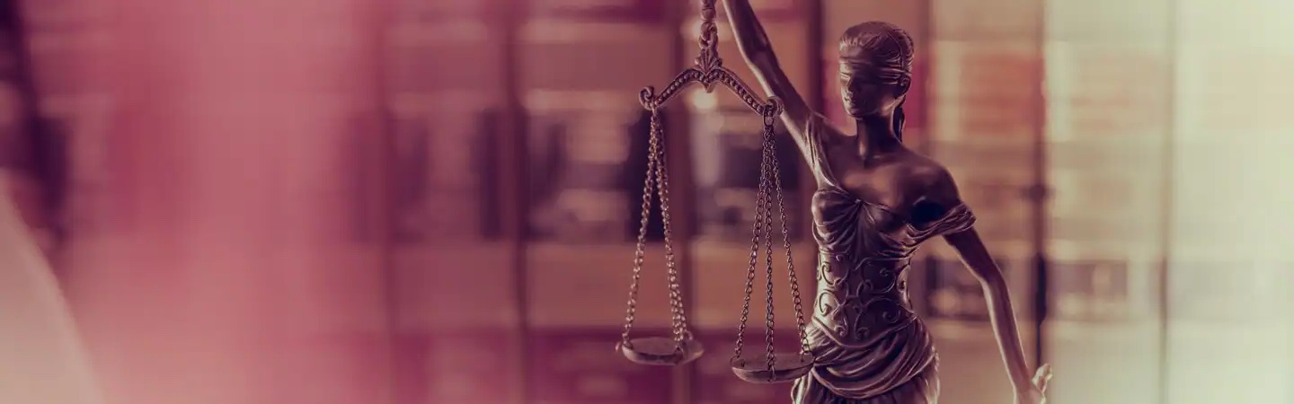 Statue of Lady Justice holding scales, with bookshelves blurred in the background.