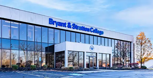 Bryant & Stratton College building with large windows under a blue sky, reflective glass, and surrounded by shrubbery.