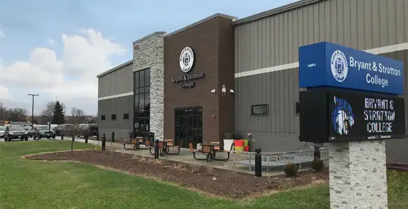 Exterior view of Bryant & Stratton College building with a signboard and benches in front.