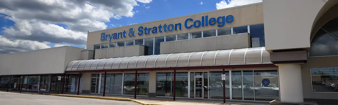 Front exterior of Bryant & Stratton College building with glass entrance under a blue sky with clouds.