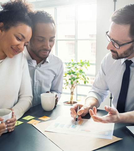 A couple sits with a business professional, discussing documents. All are smiling and holding coffee cups.
