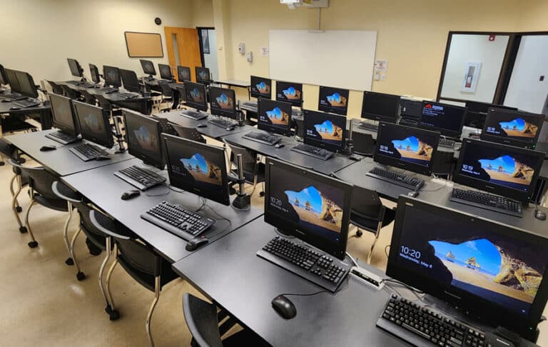 A modern computer lab with rows of desktop computers and monitors displaying Windows login screens.