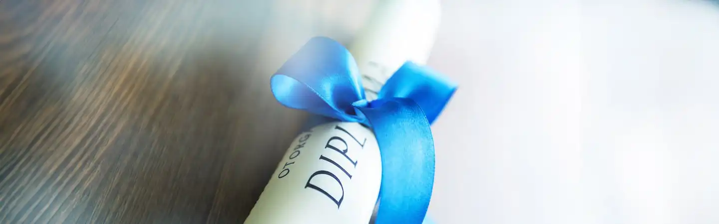 A rolled-up diploma tied with a blue ribbon, laid on a wooden surface.