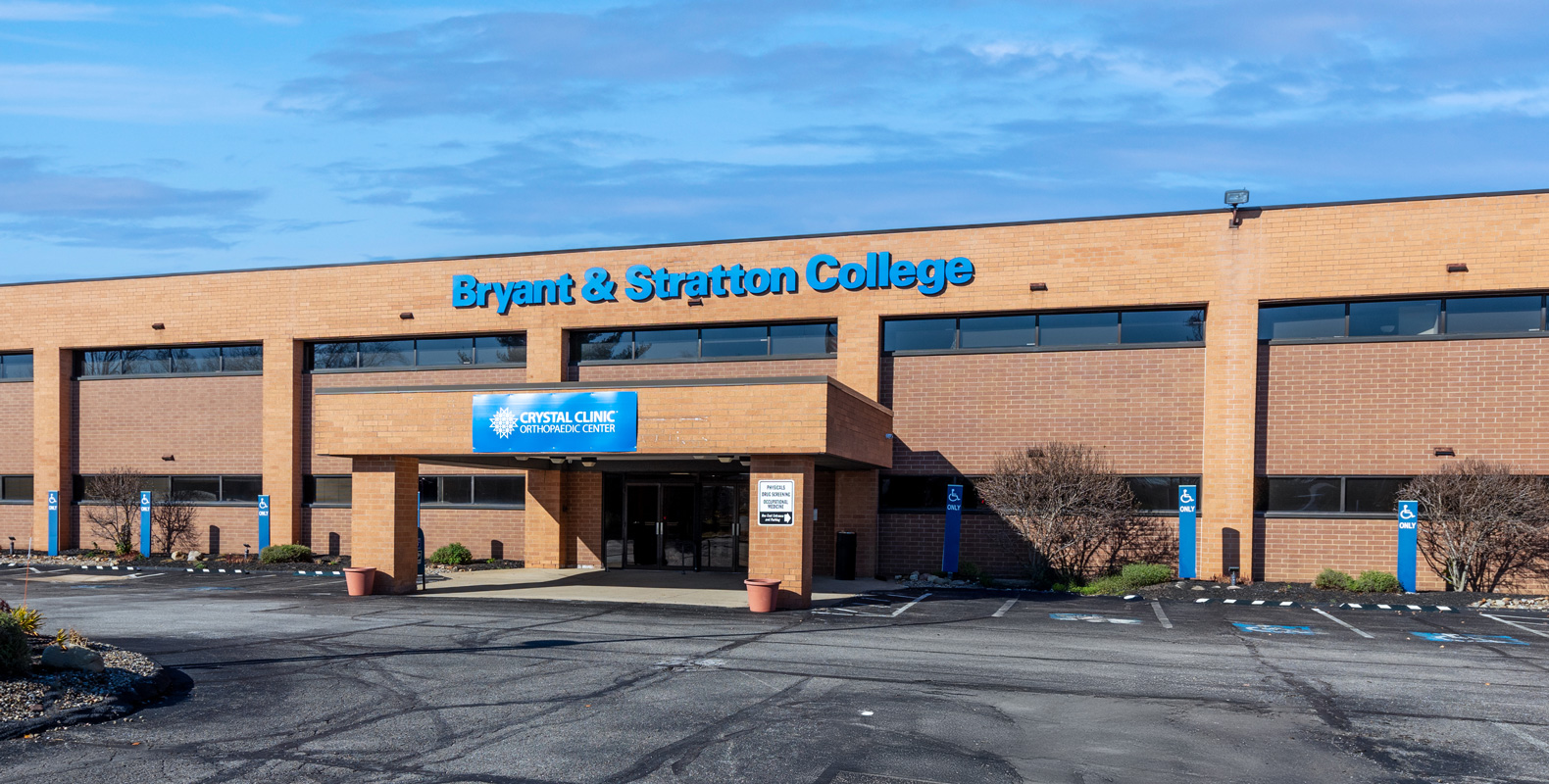 A two-story brick building with a sign reading "Bryant & Stratton College" above the entrance. This Ohio college features a blue awning at the entrance and several accessible parking spaces in front.