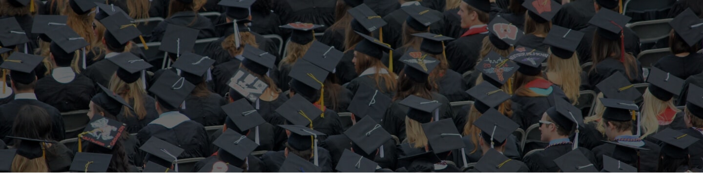 A crowd of graduates wearing caps and gowns, seated at an outdoor graduation ceremony.