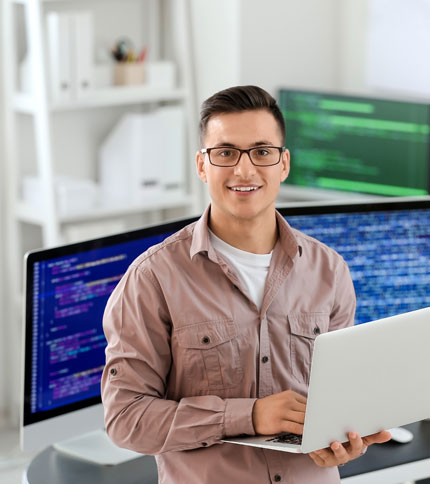 A young IT specialist holding a laptop in a tech workspace.