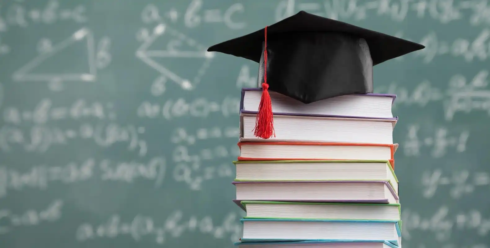 Stack of books with a graduation cap on top, against a chalkboard filled with mathematical formulas.