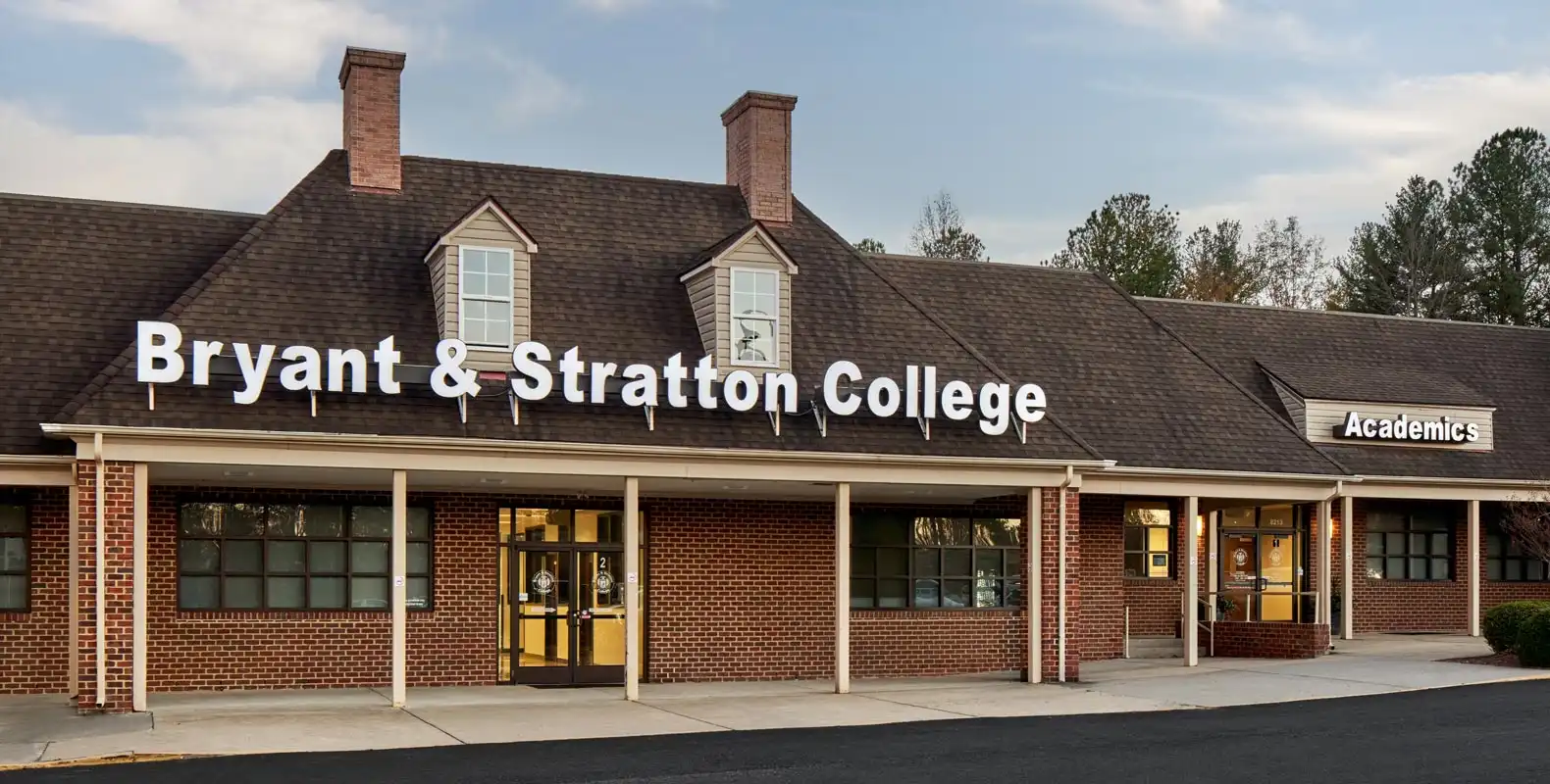 A brick building with "Bryant & Stratton College" and "Academics" signs on the roof and windows.