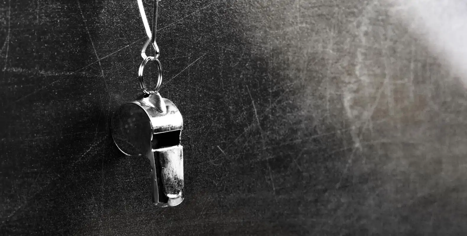 A metal whistle hanging by a string against a dark, textured background.
