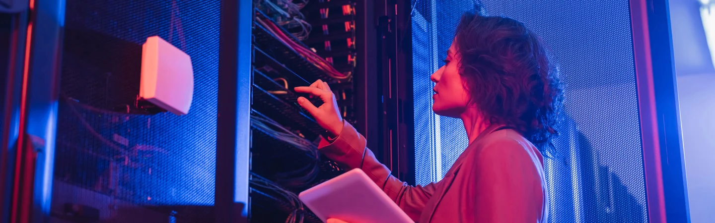 A person using a stylus and tablet while working on servers, illuminated by blue and pink lights.