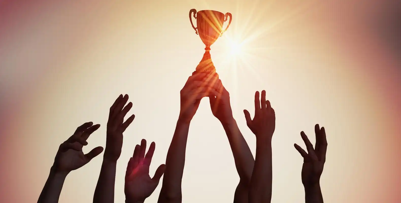 Several hands raised toward a glowing trophy against a bright sky, with the sun creating a radiant effect around the cup.