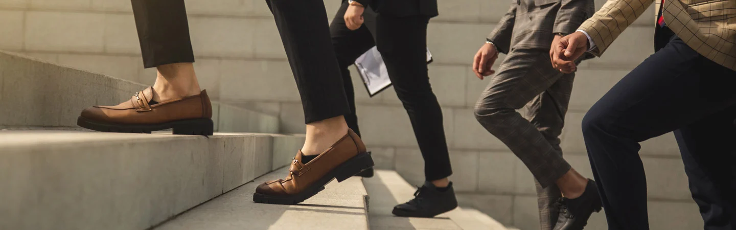 Four people in business attire ascending concrete steps, focusing on their legs and shoes.