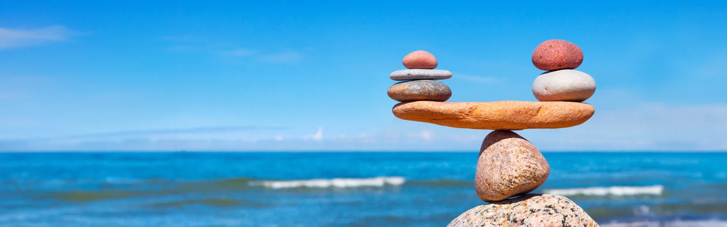 Stacked balanced stones on a beach with blue ocean waves and clear sky in the background.