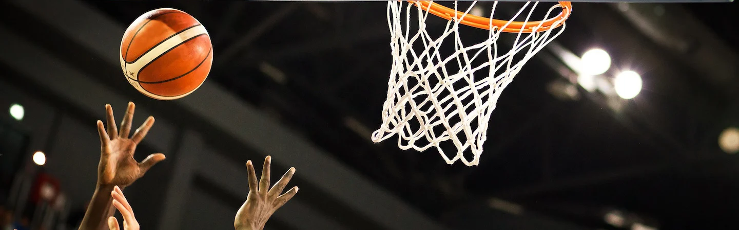 Basketball flying towards the hoop with outstretched hands attempting to block or shoot in an indoor court setting.