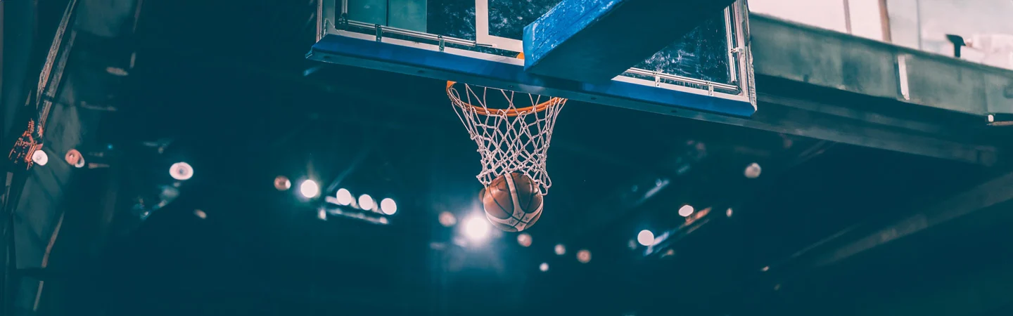 A basketball falling through the hoop on an indoor court, with stadium lights illuminating the background.