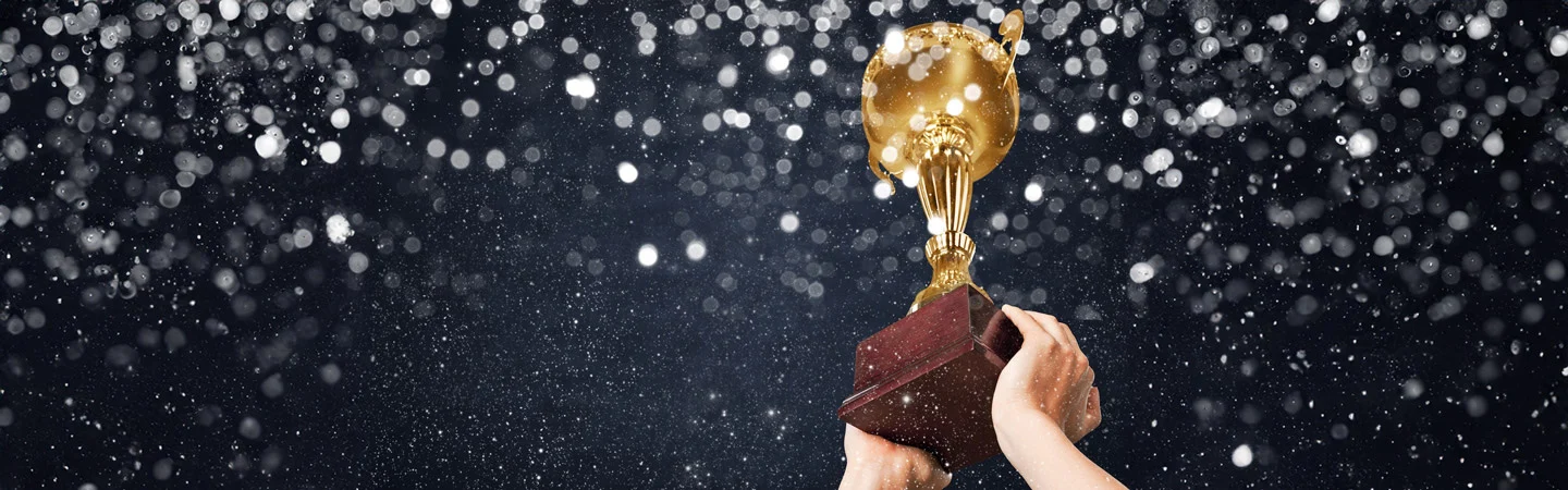 Hands holding up a golden trophy with a dark, glittering background.