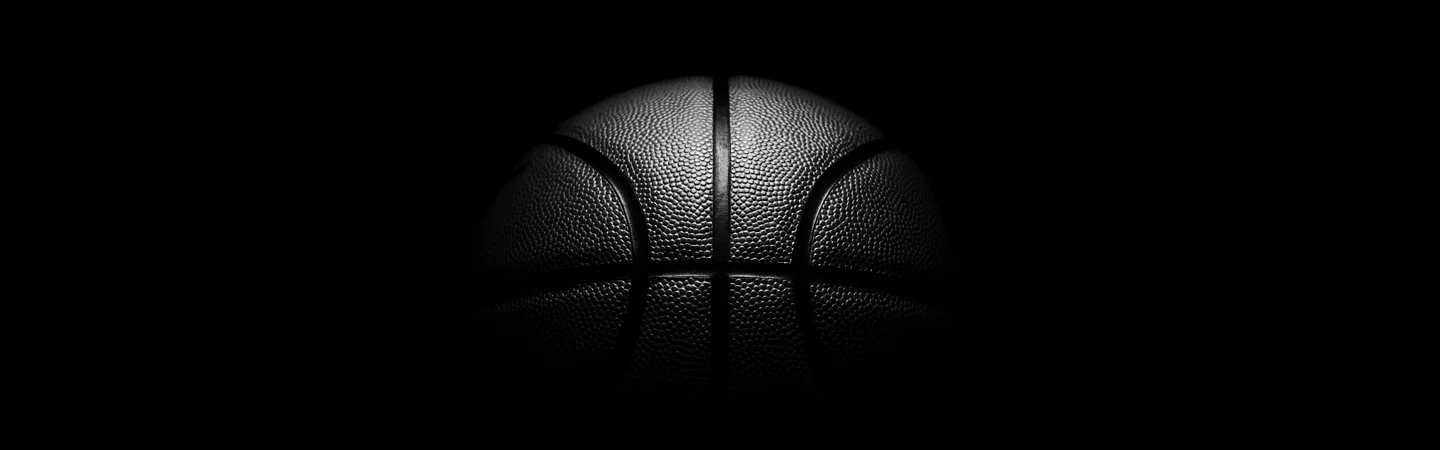 A basketball partially illuminated from above, set against a dark, shadowy background.