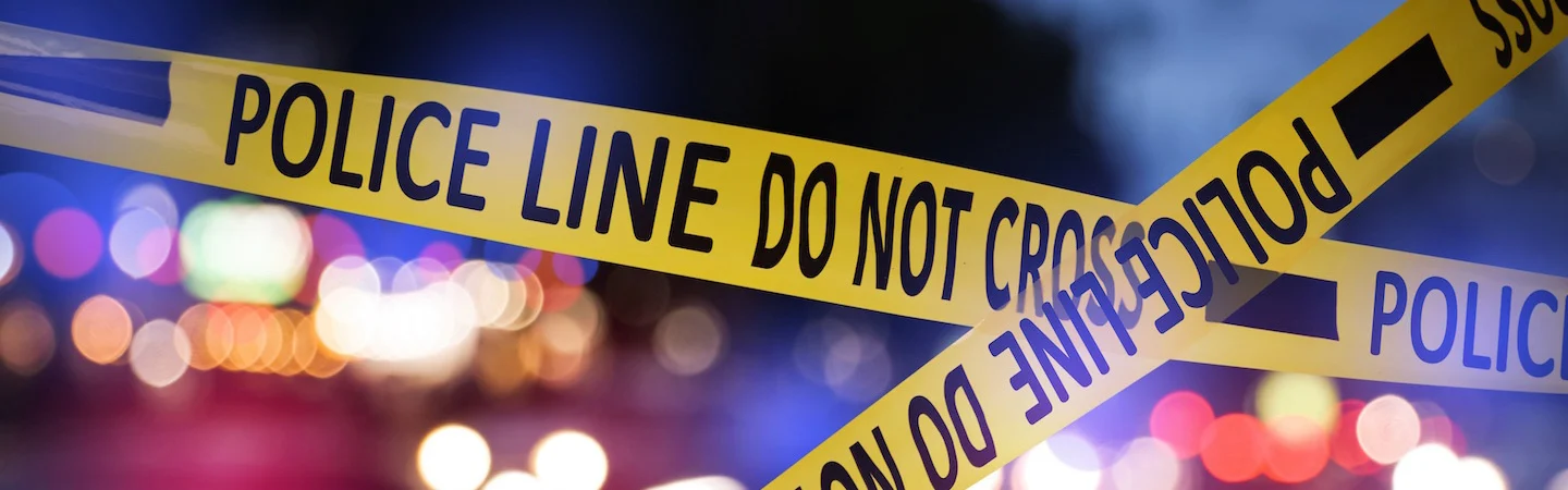 Yellow police tape with "Police Line Do Not Cross" text, blurred colorful lights in the background.