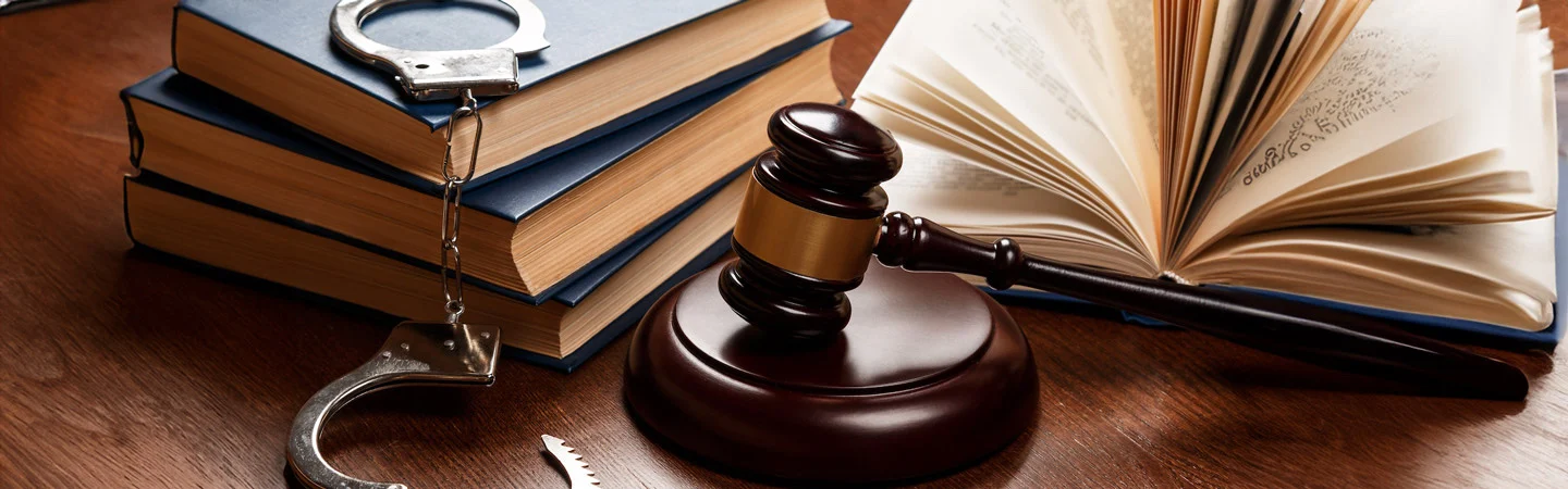 Gavel, handcuffs, and books on a wooden desk, symbolizing law and justice.