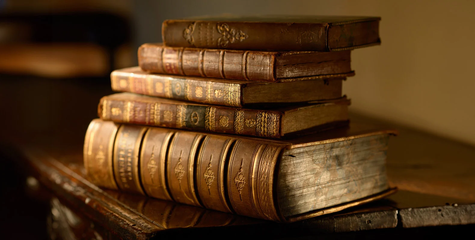 A stack of five old, weathered books with ornate bindings placed on a wooden table.