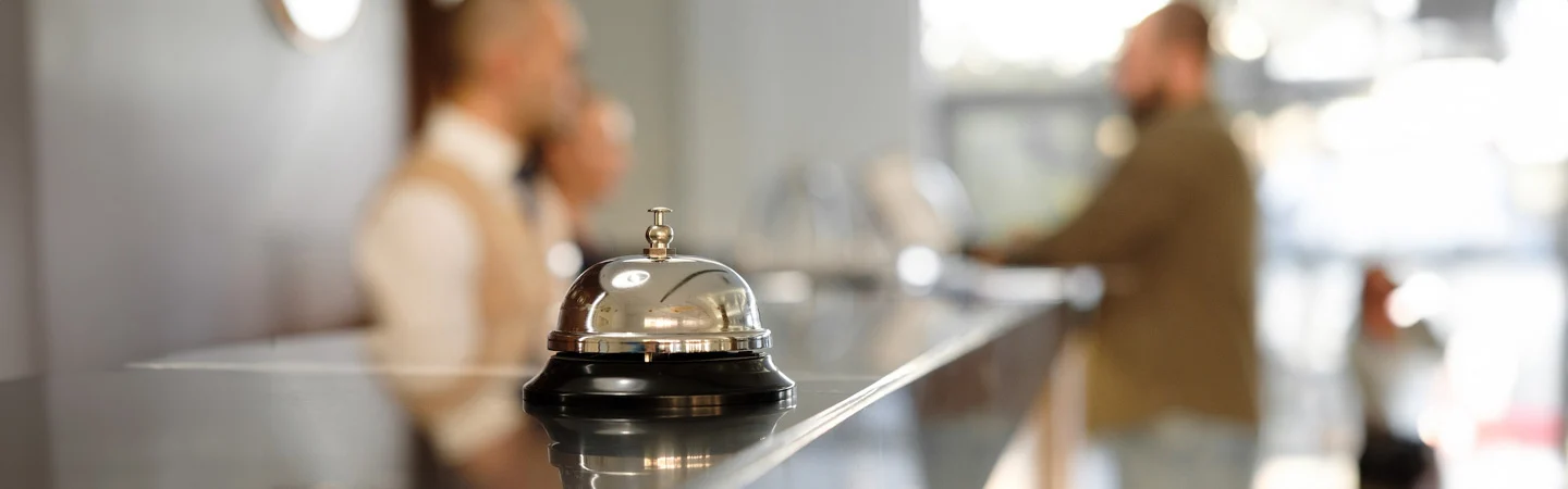 Close-up of a hotel bell on a counter with two blurred people talking in the background.