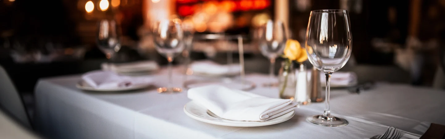 Elegant restaurant table setting with white tablecloth, wine glasses, and neatly folded napkins.