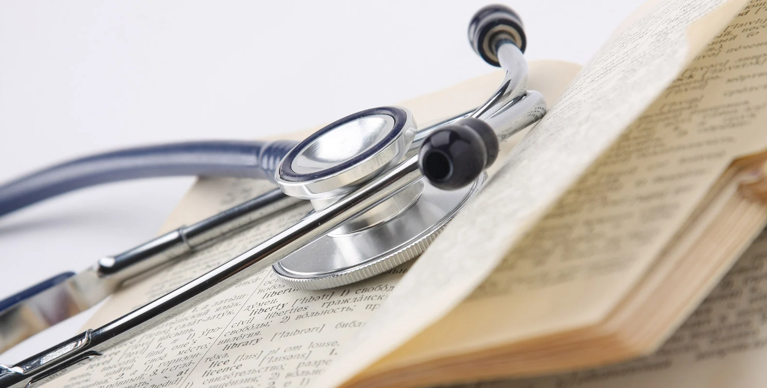 A stethoscope resting on the open pages of a medical textbook.