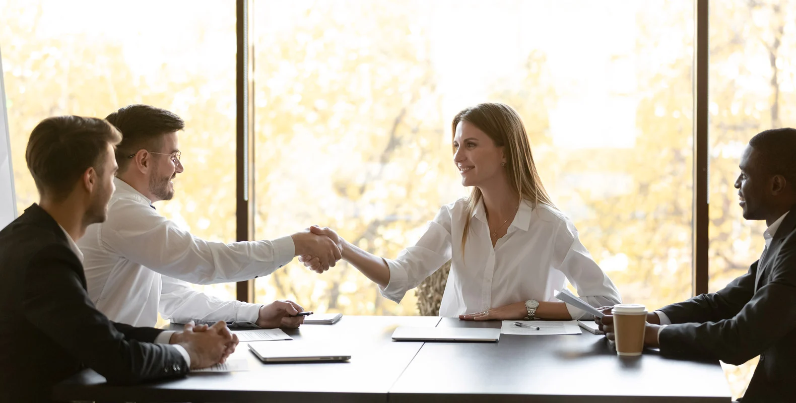 Four professionals sit around a table, with two of them shaking hands and smiling during a meeting.