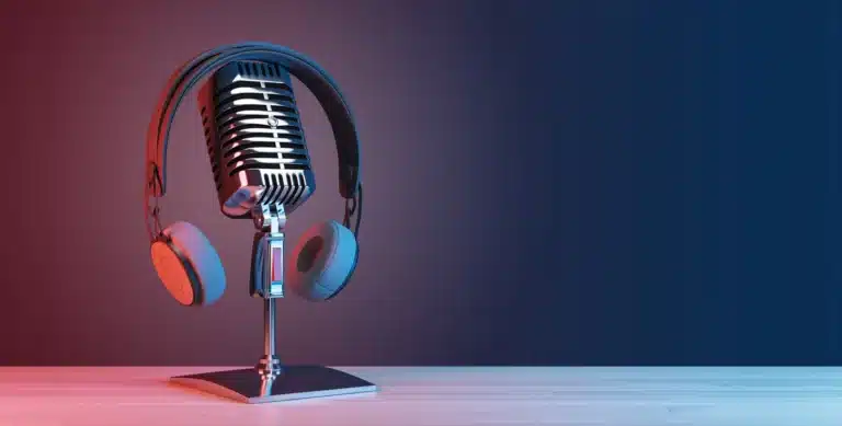 Vintage microphone with headphones placed around it, set on a stand against a gradient red to blue background.