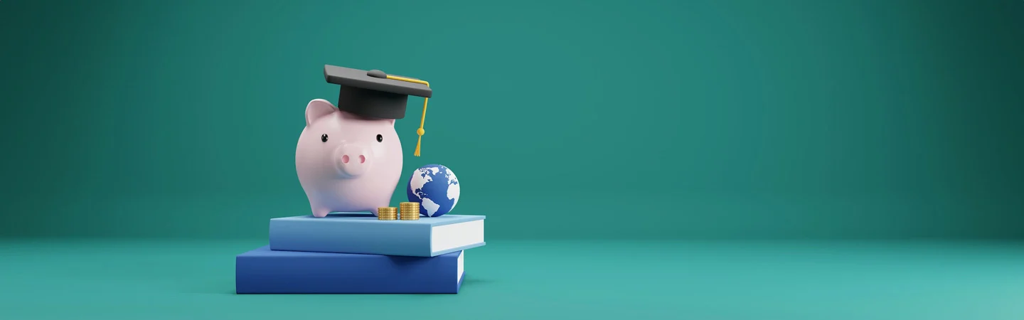 Piggy bank wearing a graduation cap, placed on stacked books beside a small globe and coins on a teal background.