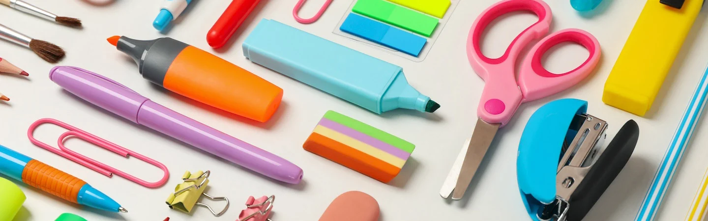 An assortment of colorful office and school supplies, including pens, scissors, sticky notes, and a stapler, on a white surface.