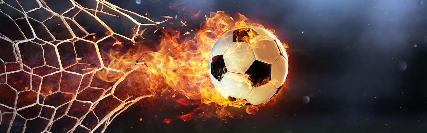 A soccer ball engulfed in flames hitting the back of a net, leaving a fiery trail.