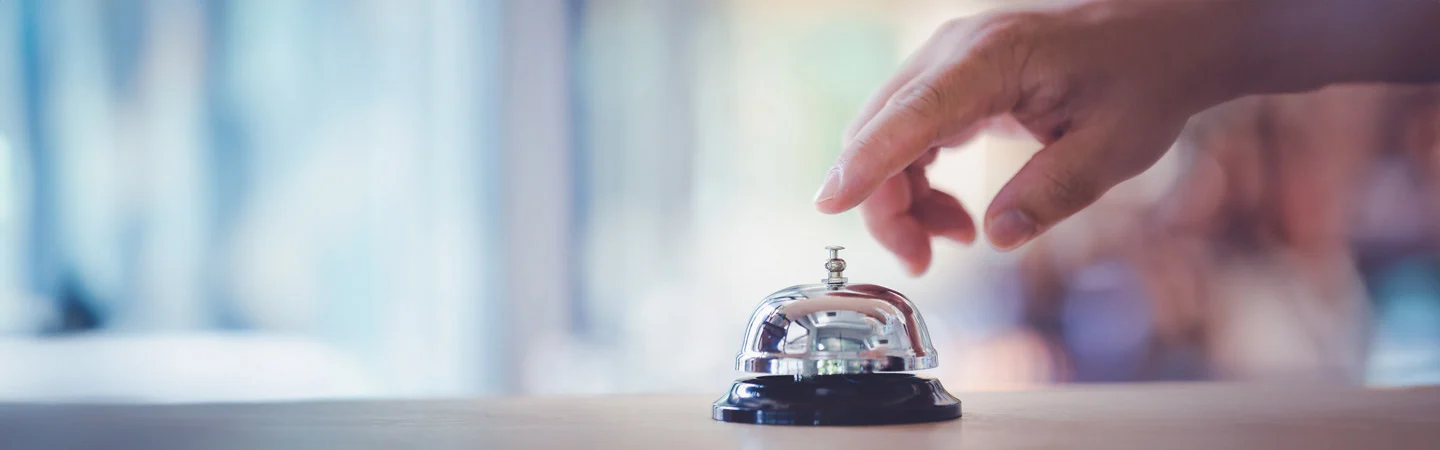 A hand about to ring a service bell on a counter with a blurred background.