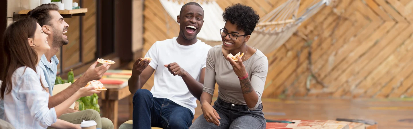 Four people sitting outdoors, smiling and laughing while eating pizza.
