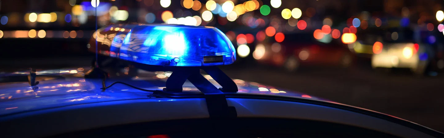 Police car with blue flashing lights on at night, city lights and blurred vehicles in the background.