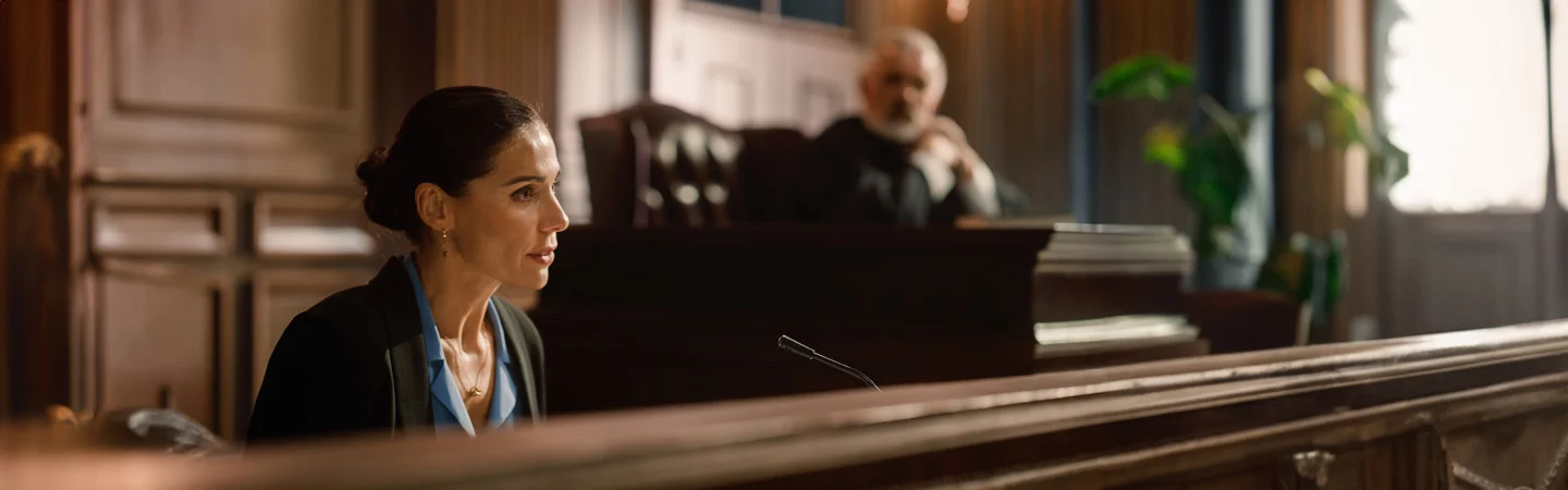 A woman is speaking in a courtroom, with a judge seated in the background.