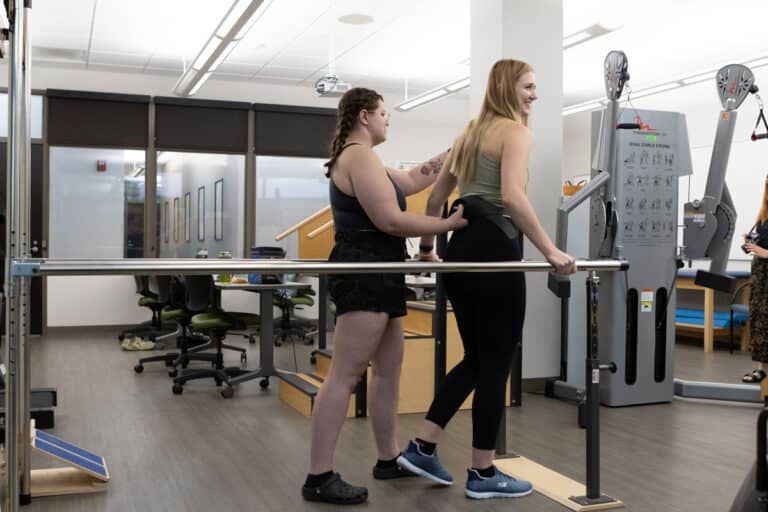 A physical therapist assists a woman using a walking rail in a rehabilitation center.