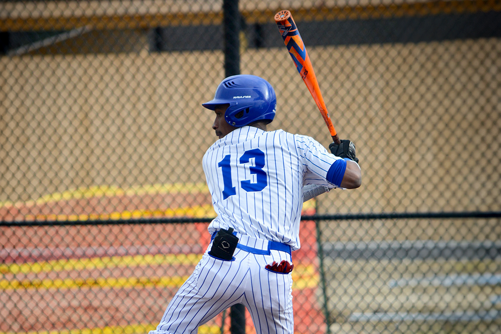 A baseball player in a blue pinstripe uniform with number 13 preparing to bat, holding an orange bat.