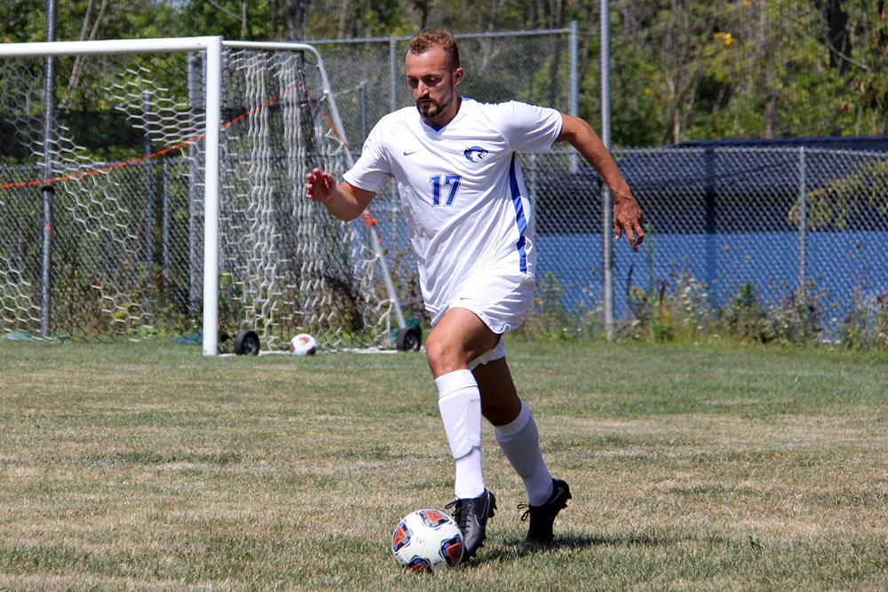 A soccer player in a white uniform and the number 17 dribbles the ball on a grassy field in daylight.