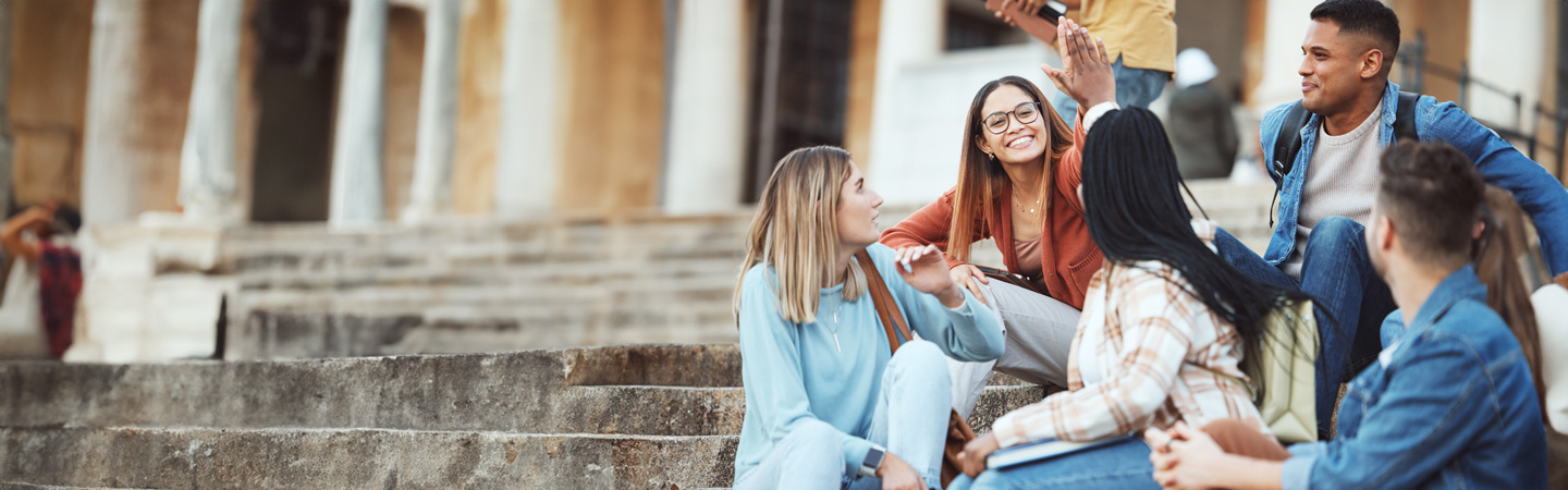 A group of young adults sitting on outdoor steps, talking and laughing together.
