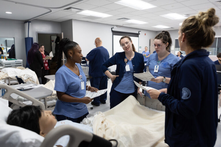 Medical professionals in scrubs discussing patient care around a hospital bed in a clinical setting.