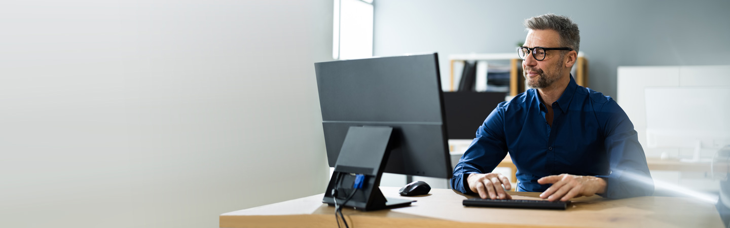 A man with glasses working on a computer in a modern office.