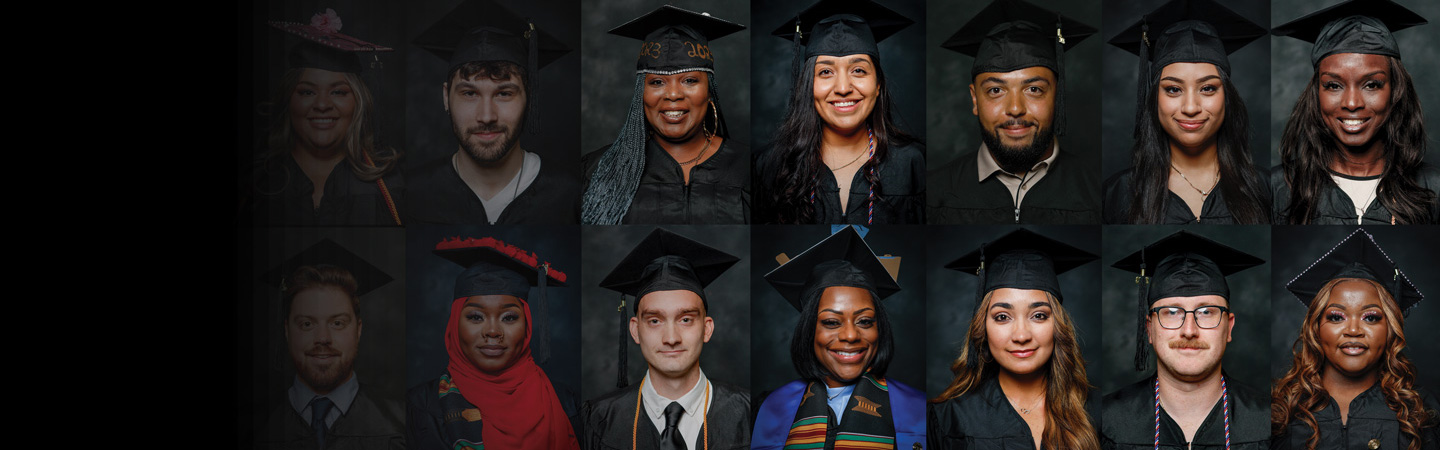A diverse group of 14 graduates in caps and gowns, smiling and standing in three rows against a dark backdrop.