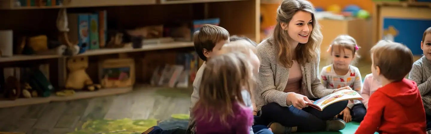 A woman reads a book to a group of young children sitting in a circle in a classroom or daycare setting.