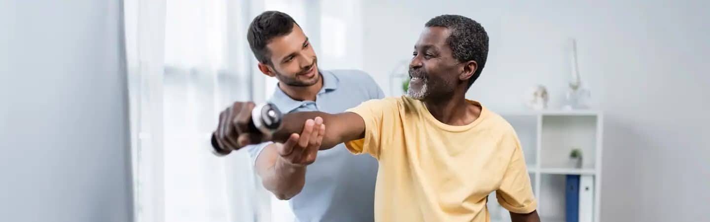 A physical therapist helps an elderly man with a stretching exercise in a bright, minimalist room.