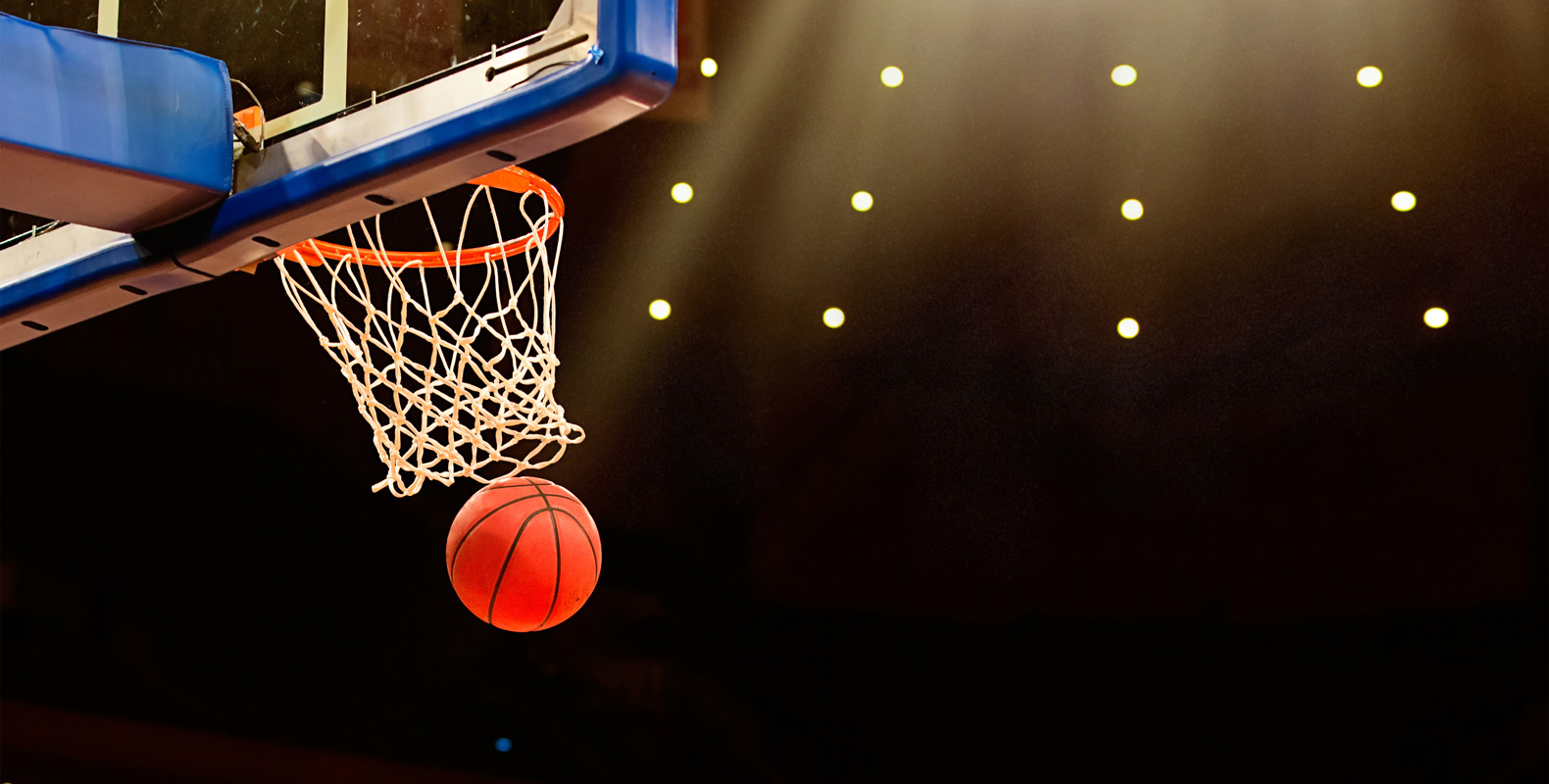 A basketball is about to go through a hoop during a game under stadium lights.