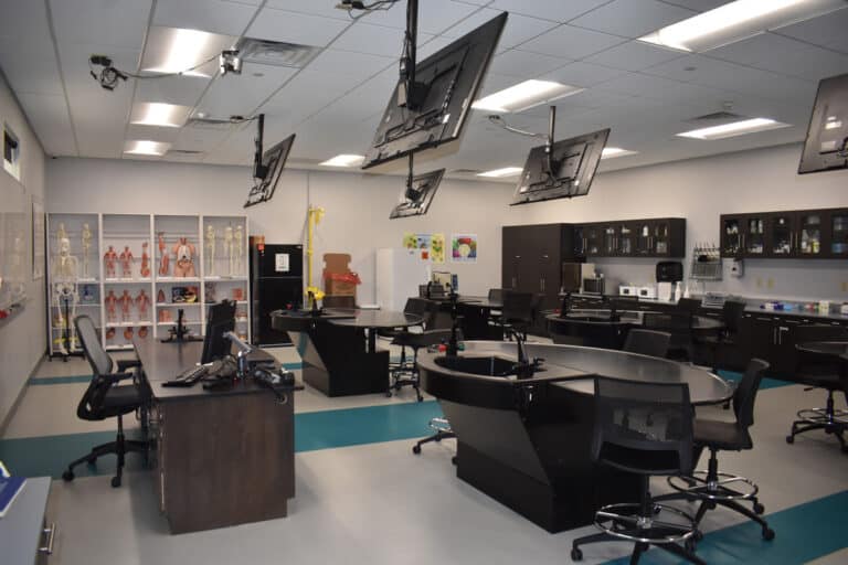A modern science classroom with multiple workstations, displays, skeletal models, and anatomical models on shelves.