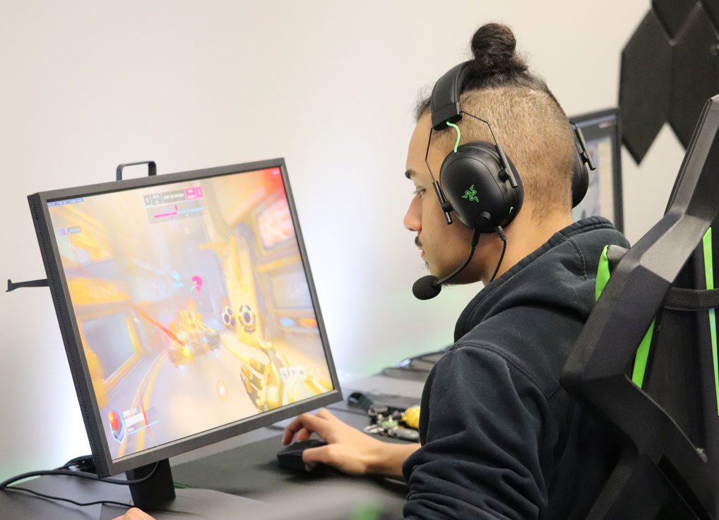 Person with headphones playing a video game on a computer in a gaming setup.