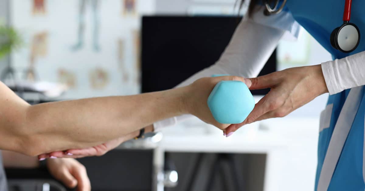 A healthcare professional assists a patient with a blue hand weight in a medical setting.